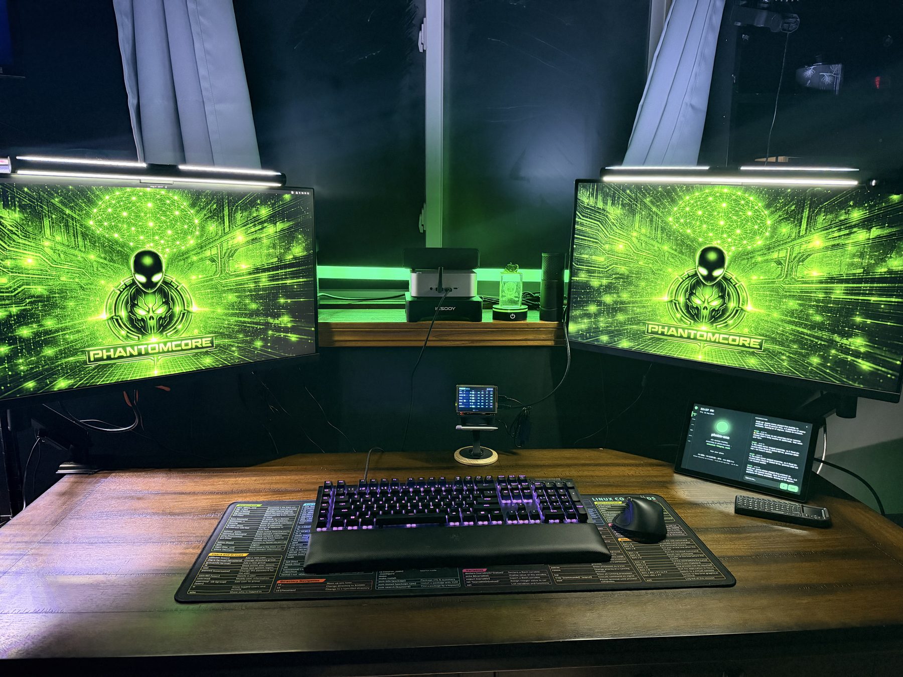 Closer view of the build desk — the phntm-one prototype's face visible on the right, a small fleet status display in the center