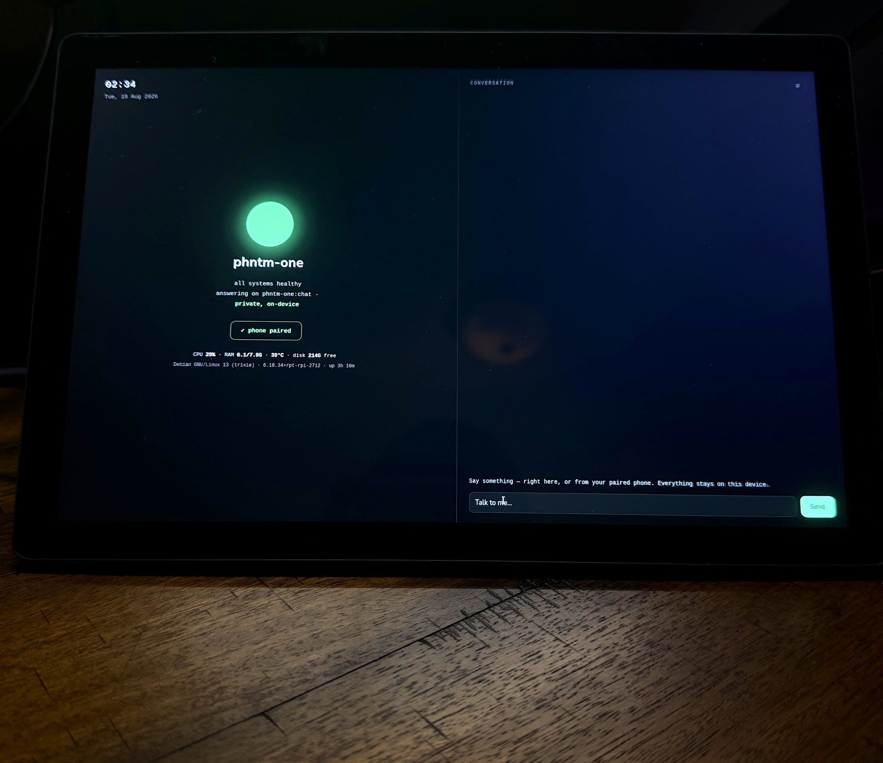 PHNTM One powered on, its green status orb glowing, on a wooden desk in a dim room